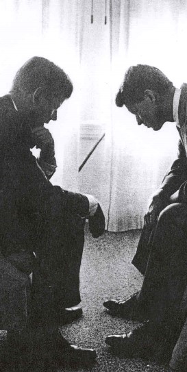 An image of John F. Kennedy and Robert F. Kennedy, sitting facing one another and looking forwards the floor.