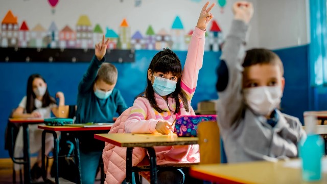 Children raising their hands while sitting at their desks in a classroom